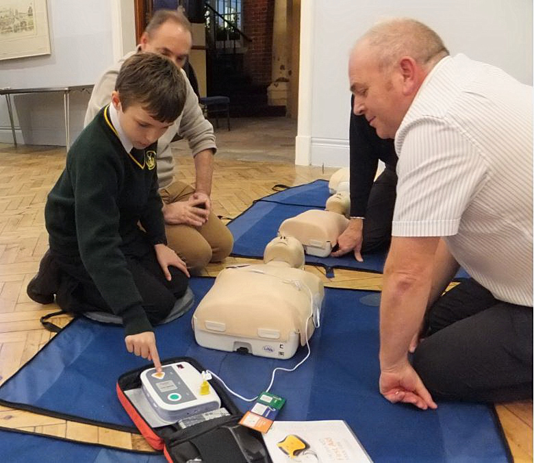 Keith Marshall watching a young man use the training defibrillator