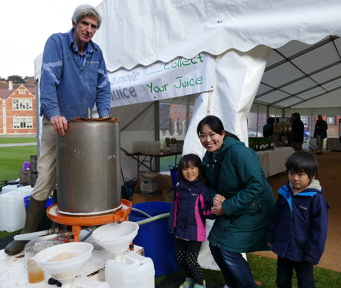 Richard Paget of My Apple Juice showing Mioka, Auto and Satsuki Honda from Royal Wootton Bassett how to turn apples into juice at Sunday's Feast of Food