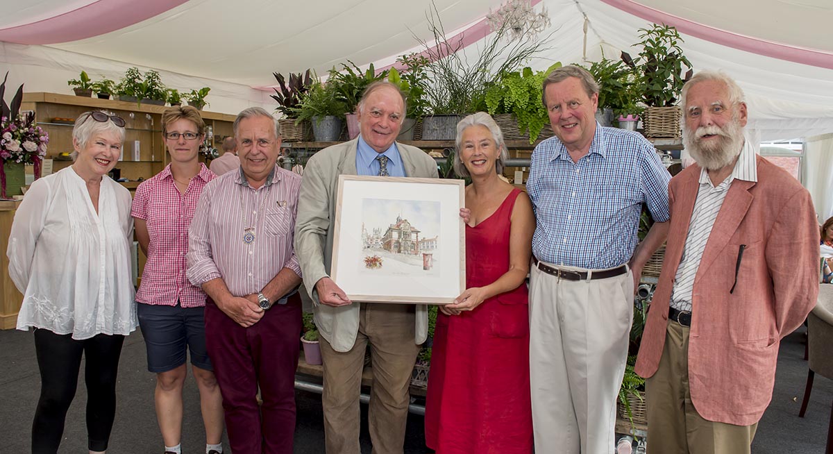 Nick Fogg, on behalf of the Town Council presents outgoing College Master Jonathan Leigh and his wife, Emma, with a signed limited edition print of the Town Hall (l-r: Edwina Fogg, Dr Janneke Blokland (Assistant Chaplain), Mervyn Hall, Nick Fogg, Emma Leigh, Jonathan Leigh and Cllr Brian Castle)